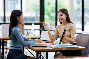 Wall Mural - Two asian female creative agency casual meeting discussion working with laptop, analyze planning and financial statistics and investment market at office.
