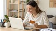 © engincan - Happy office manager shopping online, browsing web stores, buying annual mobile app membership spending her salary holding orange credit card in hand