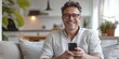 © Georgii - Middle-aged man enjoying smartphone on a cozy sofa at home