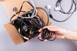 © svittlana - Womans hands holding bundle of old electronic accessories next to cardboard container, highlighting the importance of recycling electronic waste