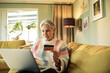 © Marko Geber - Smiling senior woman online shopping with credit card and laptop at home