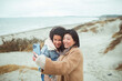 © Davor - Two female friends taking a selfie at the beach on a cold day