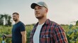 © Hafazho - Two Young Men Standing Confidently in a Lush Green Field During Golden Hour, One Man Wearing a Cap and Plaid Shirt, Agricultural Background, Blue Sky Above