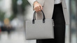 © VERTEX SPACE - A stylish woman holds sleek gray handbag while dressed in sophisticated outfit, exuding confidence and elegance in an urban setting