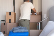 © rjankovsky - A man is standing in a room with boxes and clothes. New home concept.