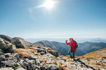 Wall Mural - Backpacker woman in bright red jacket walking by mountain range using trekking poles with Liptov valley background, Western Tatras, Slovakia. Active people and European hiking tourism concept image.