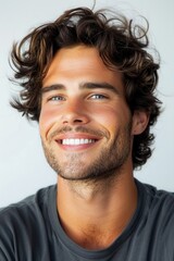 Wall Mural - Smiling young man with curly hair poses casually against a light background showcasing his bright, cheerful demeanor during a relaxed moment