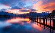 © ngamaz - Vibrant sunrise over calm lake with wooden pier.