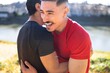 © Studio Marmellata - Two men embrace and laugh warmly near a serene riverside trail, surrounded by vibrant foliage and illuminated by golden sunlight on a clear autumn day