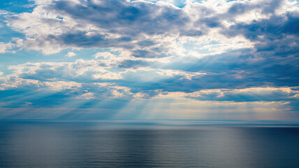 Wall Mural - Vast Calm Blue Ocean with Dramatic Sky, Fluffy White Clouds and Sunlight Rays Illuminating Water, Horizon Faintly Visible, Serene