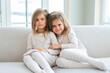 © Юлия Завалишина - Happy family sisterly love. Two funny little twin sisters girls hugging with love care playing together at home indoors. Happy children lifestyle. Identical twin girls hugs. Girls friendship and youth