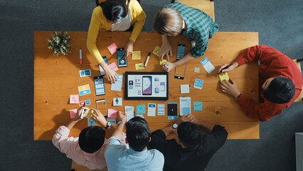 Top view of software developer team looking Ux Ui design for mobile phone interface from tablet while comparing and planning wireframe prototype designing together at creative workplace. Convocation.