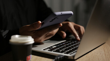 Programmer is working on laptop and holding smartphone at night