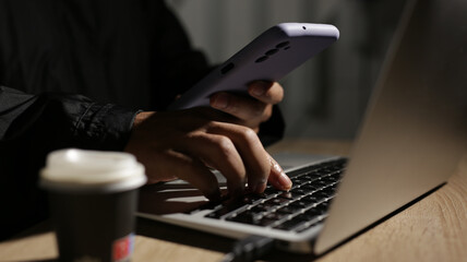 Programmer is working on laptop and holding smartphone at night