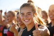 © Helen - Cheerful young athlete giving a thumbs up during an outdoor sports event with teammates in the background at sunset
