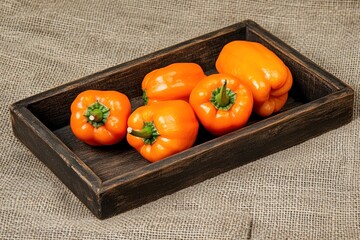 Sticker - Five ripe orange bell peppers in a rustic wooden tray on burlap.