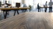 © David Giraud - Une table en bois vide en gros plan avec un arrière-plan flou de personnes travaillant dans un les bureaux d'une entreprise.