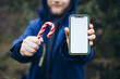 © ADDICTIVE STOCK - Man holding candy cane and smartphone with blank screen