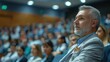 © aicandy - Side Profile of a Mature Man with Gray Hair Attentively Listening to a Speaker in a Conference Room Filled with an Engaged Audience During a Public Event