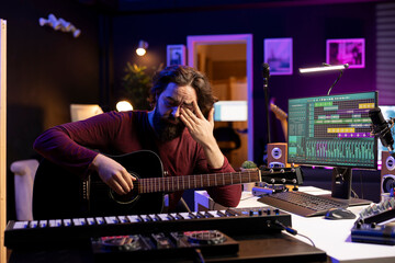 Fototapete - Frustrated artist having lack of inspiration in finishing song on acoustic guitar, thinking of accords to play and create a masterpiece. Musician being tired and displeased with recorded tunes.