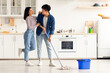 © Prostock-studio - Beautiful loving asian young couple mopping floor in kitchen together, full length photo, copy space. Romantic cheerful chinese lady hugging her smiling boyfriend while cleaning house