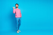 © deagreez - Confident man pointing to the side wearing casual pink sweater and blue jeans on a vibrant blue background