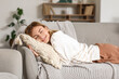 © Pixel-Shot - Young woman with pillow resting on grey sofa at home
