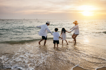 A carefree day at beach for an Asian family. Parents and daughters seen from behind enjoy bonding moments playing running and pretending to fly with arms outstretched. Family joy in sunlight.