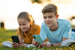 © bilanol - Happy teenagers girl and boy browsing social media on their cellphones in summer park.