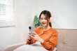 © Fahng - Happy asian woman listening to music from mobile phone sitting on a couch at home. Smiling girl relaxing with headphones in morning, Time to relax. copy space.