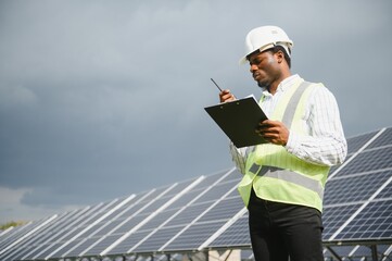 Wall Mural - Construction site African worker wearing safety vest and helmet holding a radio, solar panel