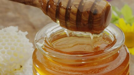 Wall Mural - Drops of honey slowly flowing from a wooden honey dipper into a honey bowl, close-up, slow motion.