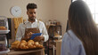 © Krakenimages.com - Man in apron using tablet across countertop with pastries while woman waits in bakery interior