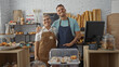 © Krakenimages.com - Woman and man bakers wearing aprons smiling and posing together in a cozy bakery interior filled with breads and pastries.