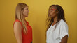 © Krakenimages.com - Women talking together against a yellow background, demonstrating friendship and interaction, one in a red top and the other in a white top.