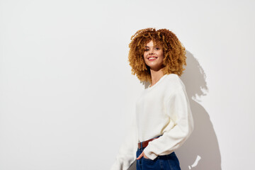 Wall Mural - Smiling woman with curly hair in a white sweater against a minimalistic white background, embodying confidence and casual style Perfect for lifestyle and fashion imagery