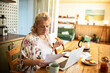 © Marko Geber - Woman reading bills with laptop on kitchen desk