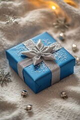 Wall Mural - vertical photo vibrant blue Christmas present box with a silver ribbon and bow placed on a snow with small shiny balls on light creamy textile background