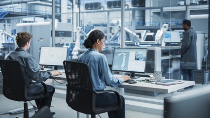 Leinwandbilder - Caucasian Male Programmer And Hispanic Female Assembly Line Operator Using Desktop Computers At Modern Factory With Robotic Arms. Diverse Colleagues Working On the Production Of High-Tech Devices.
