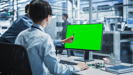 Aufkleber - Hispanic Female Manager And Asian Male Engineer Using Desktop Computer With Green Screen Chromakey On Display at Automated Factory With Robotic Arms. Colleagues Discussing Production Of Devices.