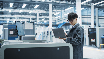 Fototapete - Asian Male Industrial Engineer Using Laptop To Control Soldering Jet Printer On Electronics Factory. Man Working On Production Of Innovative Printed Circuit Boards For Machine Learning Systems.