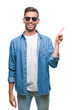 © Krakenimages.com - Young handsome man wearing sunglasses over isolated background with a big smile on face, pointing with hand and finger to the side looking at the camera.