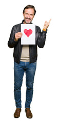 Wall Mural - Handsome middle age man holding paper with red heart very happy pointing with hand and finger to the side