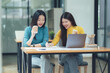 © Kritdanai - Collaborative Coffee Break: Two smiling Asian female colleagues enjoy a coffee break while working together on a project using a laptop and paperwork in a modern office setting.