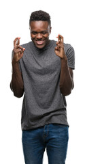 Wall Mural - Young african american man wearing grey t-shirt smiling crossing fingers with hope and eyes closed. Luck and superstitious concept.