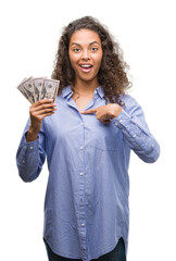 Wall Mural - Young hispanic woman holding dollars with surprise face pointing finger to himself