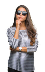 Wall Mural - Young beautiful arab woman wearing sunglasses over isolated background with hand on chin thinking about question, pensive expression. Smiling with thoughtful face. Doubt concept.