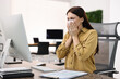 © New Africa - Sick woman with runny nose at table in office