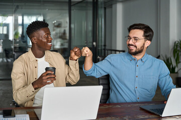 two happy diverse young professional male employees team giving fist bump at work. african and hispa