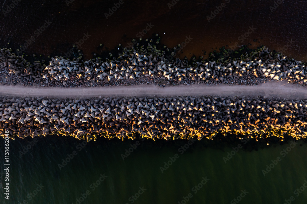 An aerial perspective of a long, narrow jetty composed of large ...